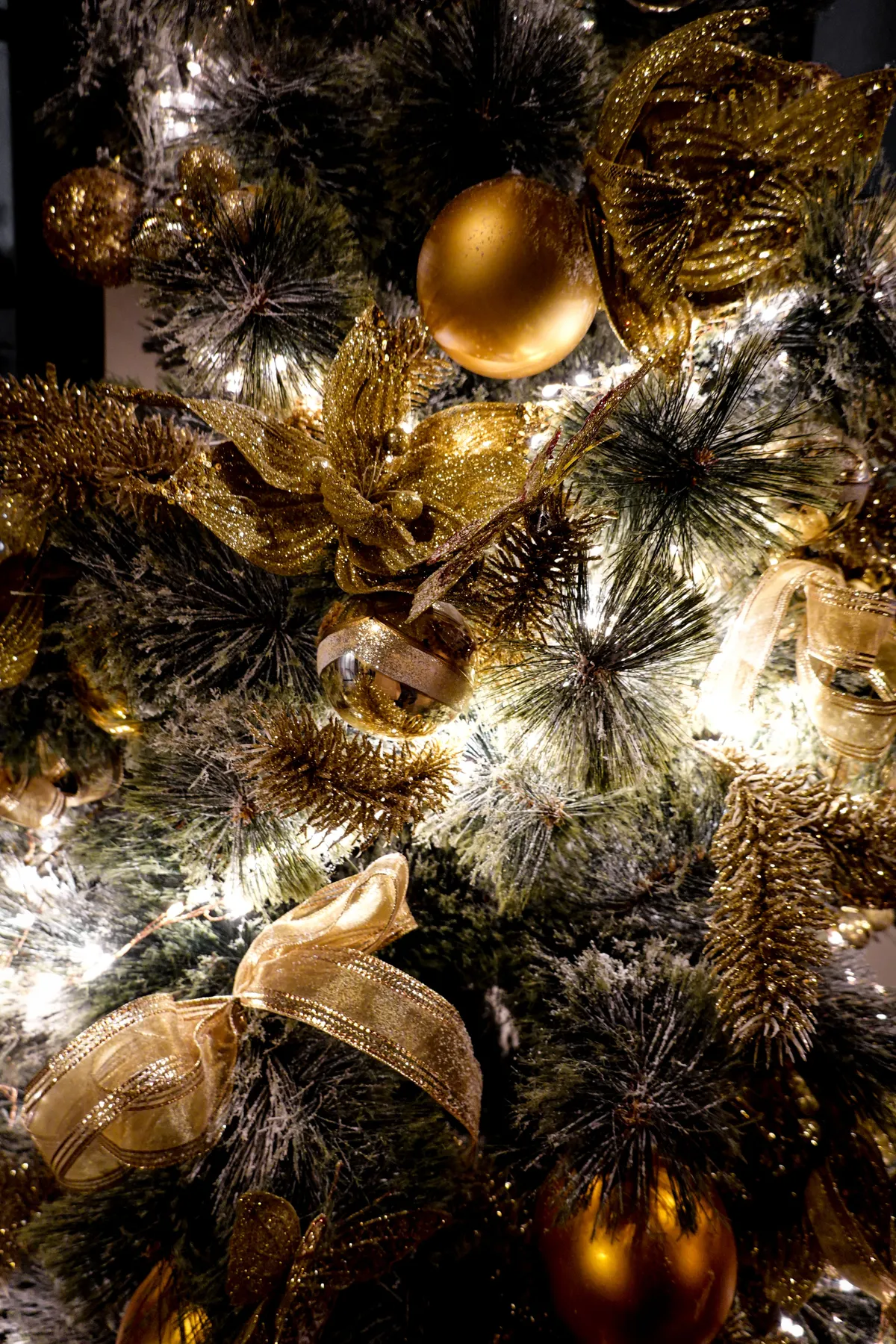A beautifully decorated Christmas tree with gold ornaments and ribbons, illuminated warmly.