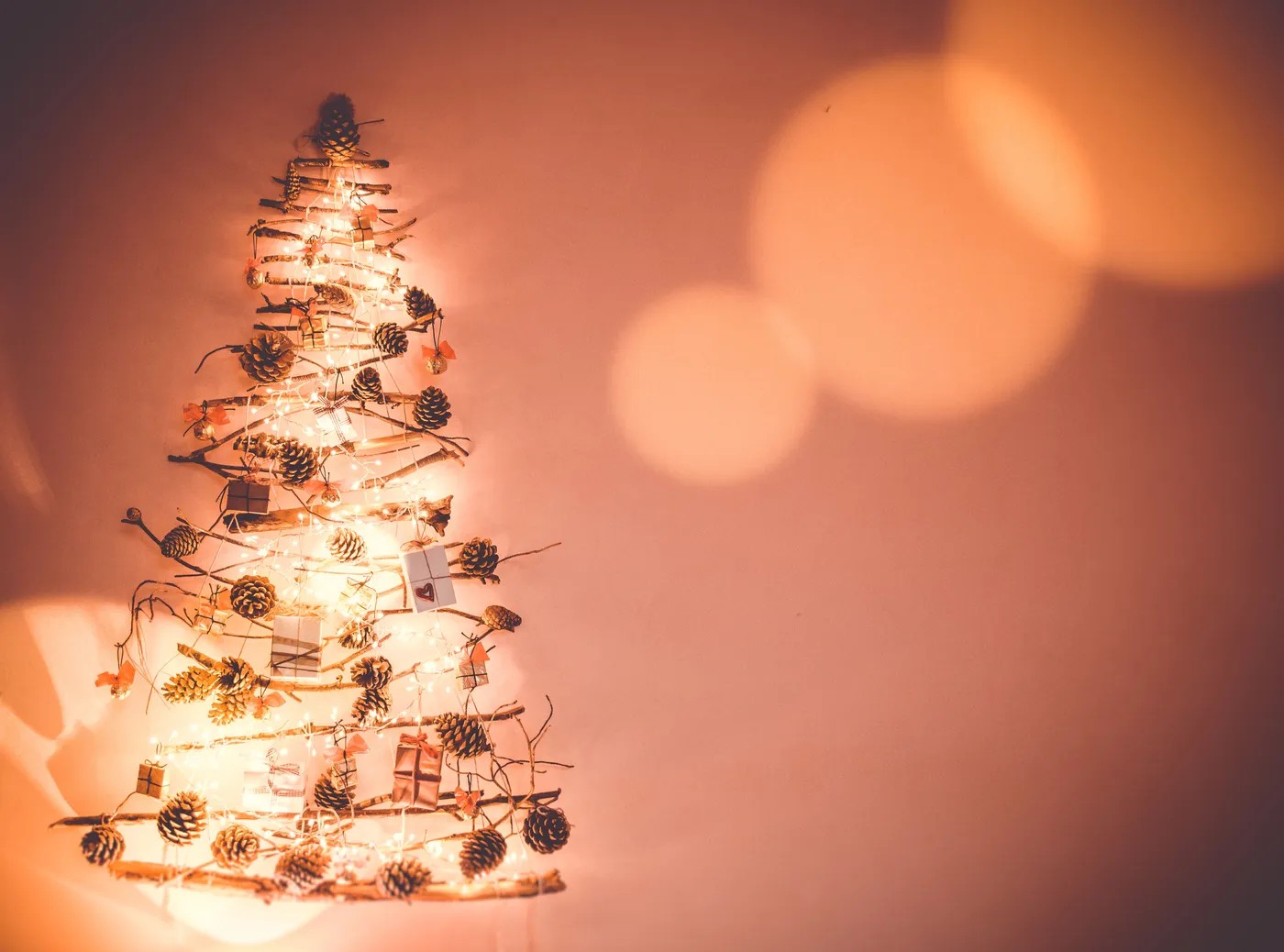 A charming minimalist Christmas tree made of pinecones and branches illuminated on a wall.