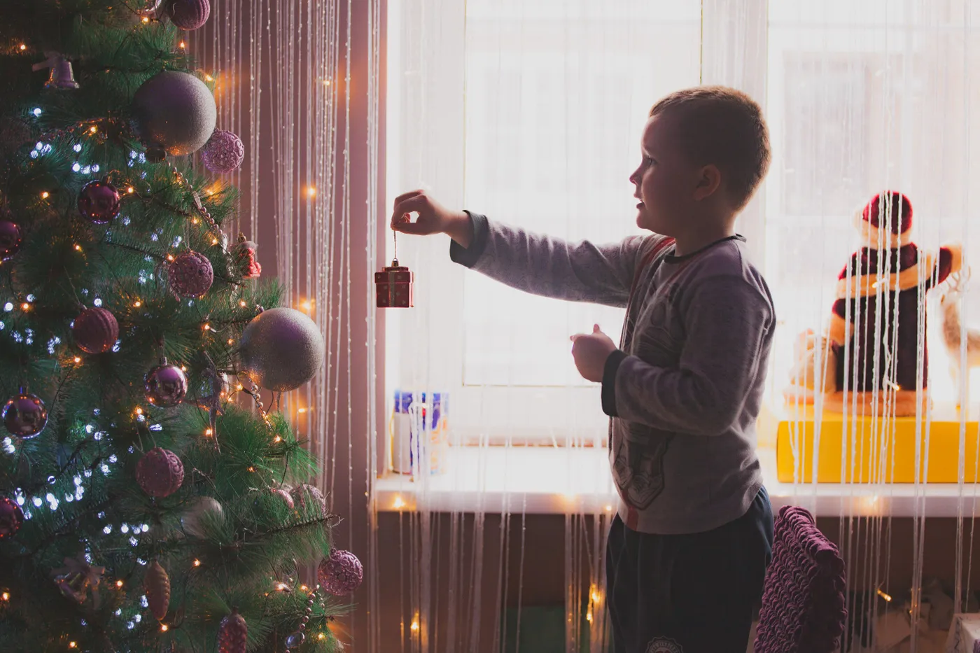 A child decorates a Christmas tree with ornaments, creating a festive holiday atmosphere.