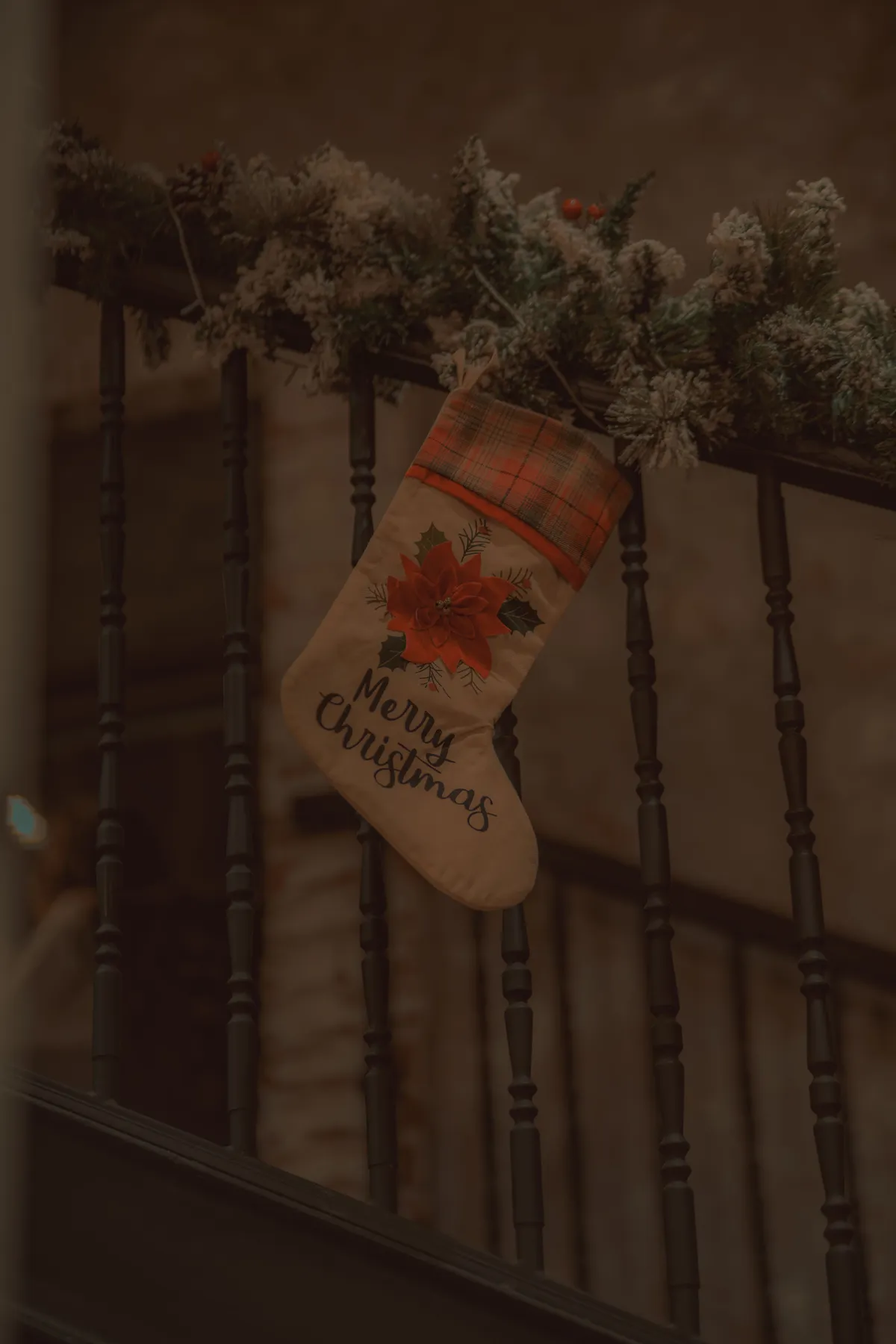 A Christmas stocking hung on a decorated railing with festive greenery indoors.