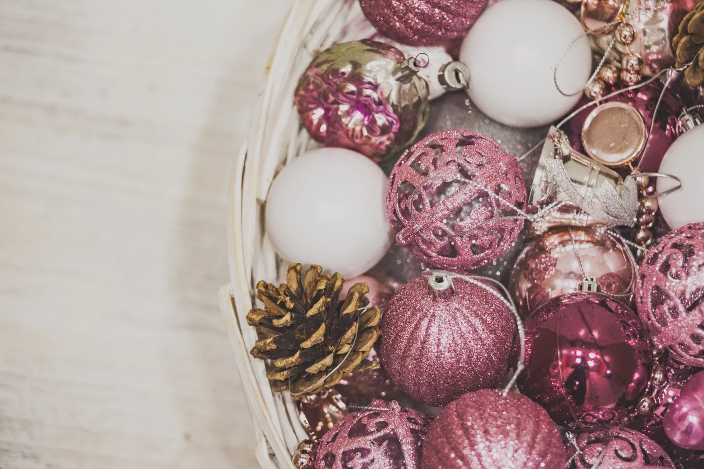 A collection of pink and white Christmas ornaments and pinecones in a basket.