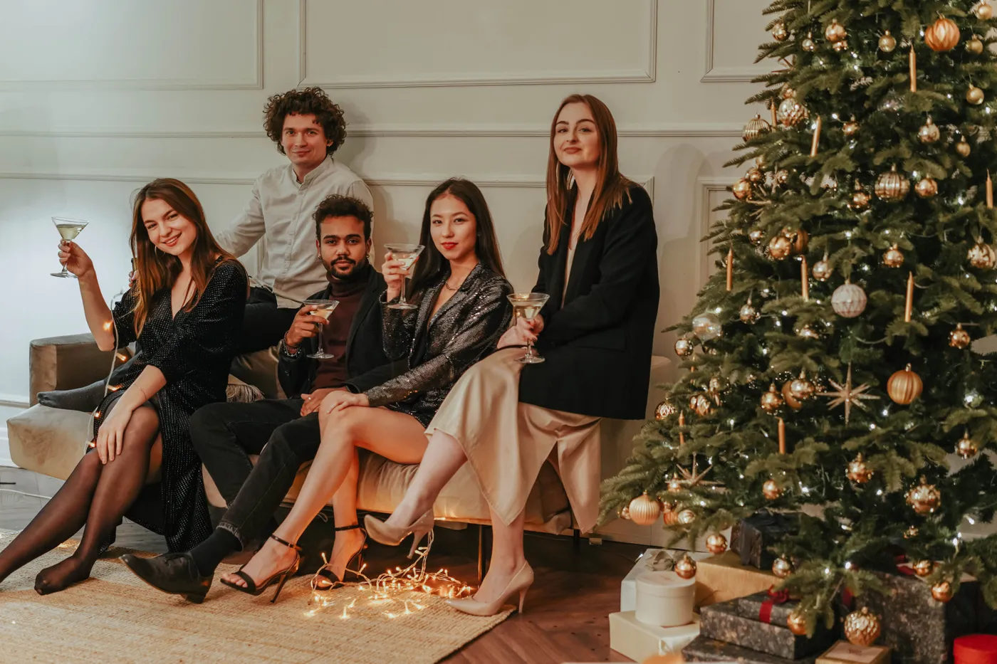 A group of adults celebrating indoors by the Christmas tree with drinks.