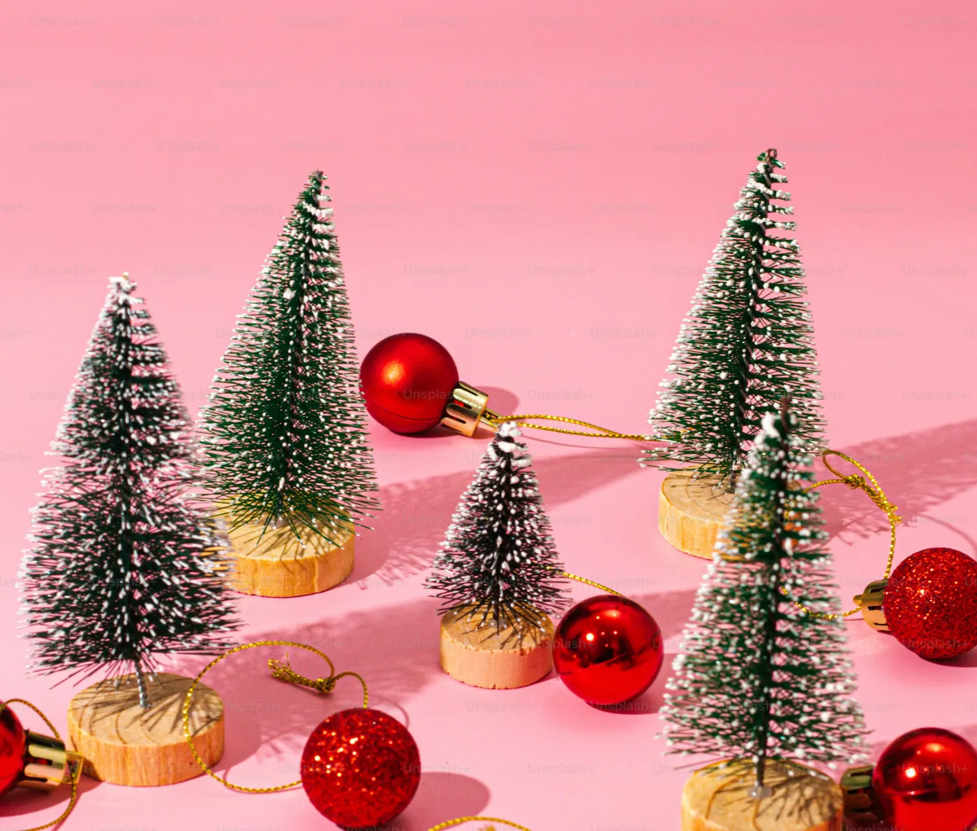 A group of small christmas trees sitting on top of a pink surface - Photo on Unsplash+