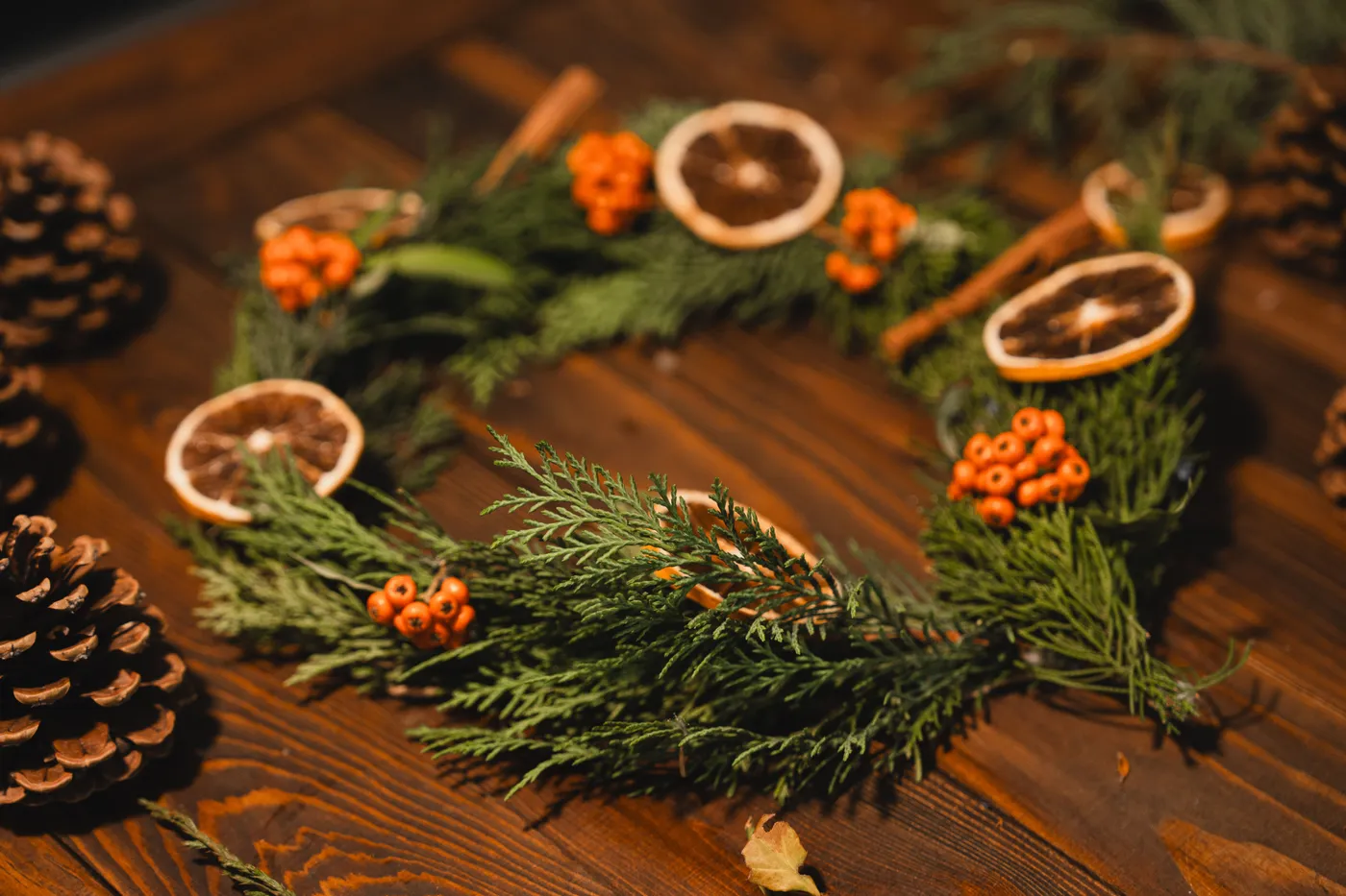 A handmade Christmas wreath with oranges and cinnamon on a wooden table.