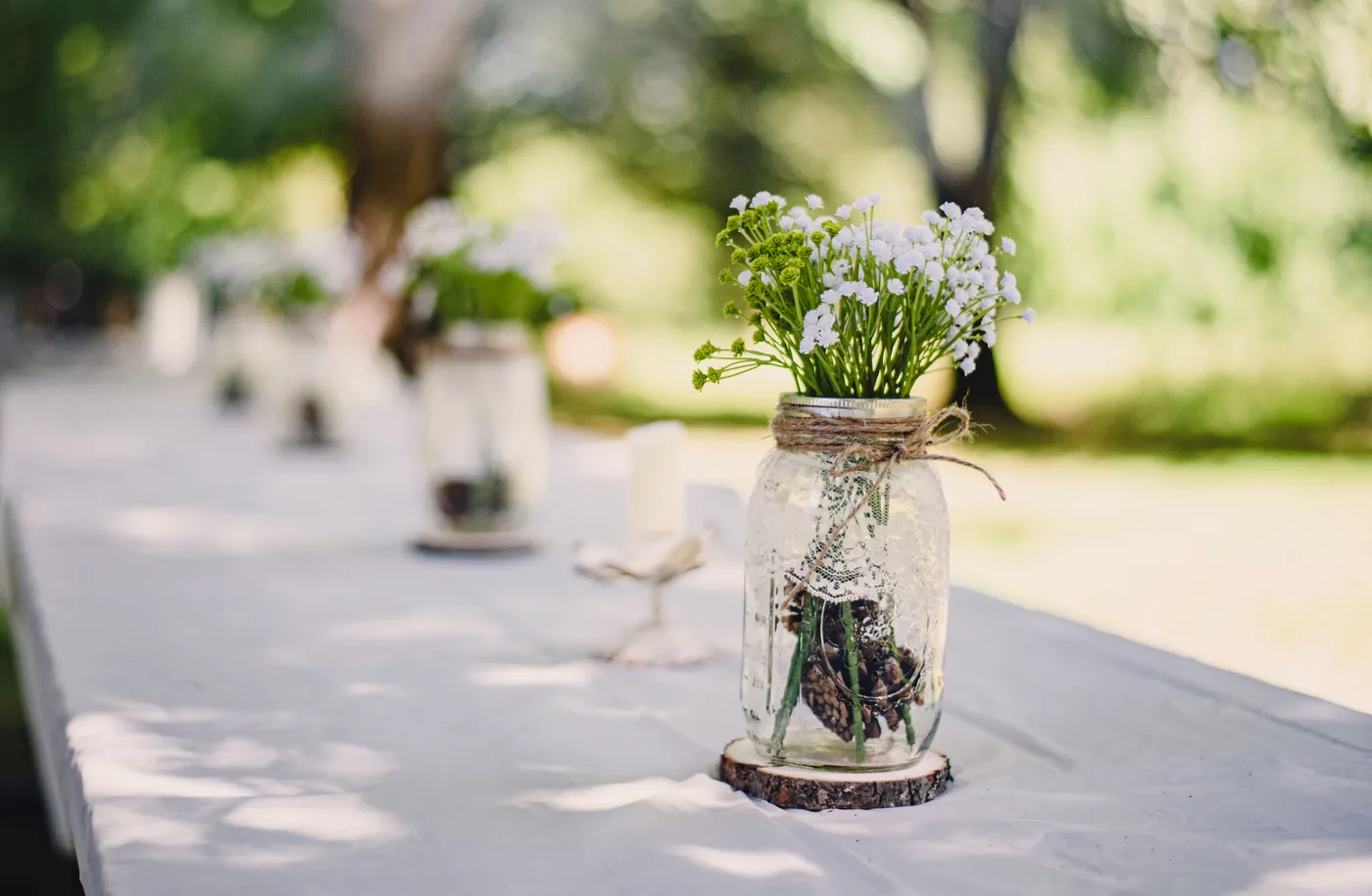 A rustic outdoor wedding table setting featuring a mason jar with wildflowers on a sunny day.