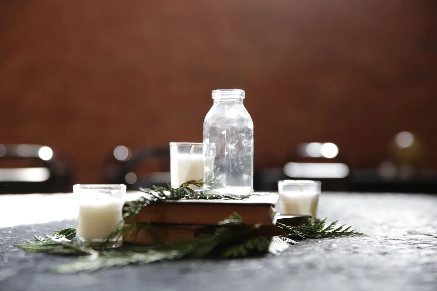 A rustic scene featuring a vintage glass bottle, candles, and greenery on a book.