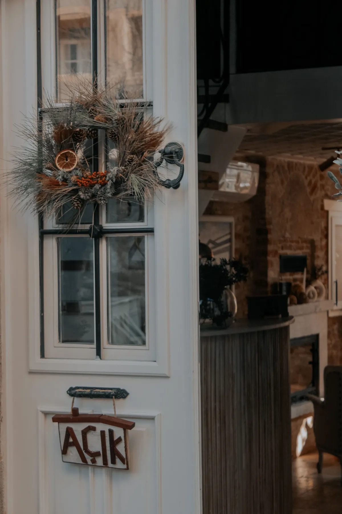 A rustic white door with a handmade wreath and 'open' sign, inviting interior view.