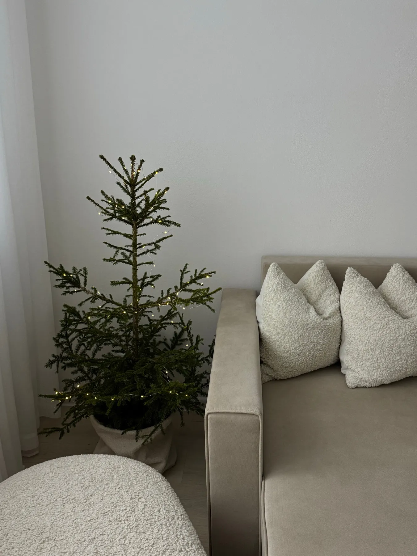 A simple Christmas tree with lights in a cozy, neutral-themed living room.