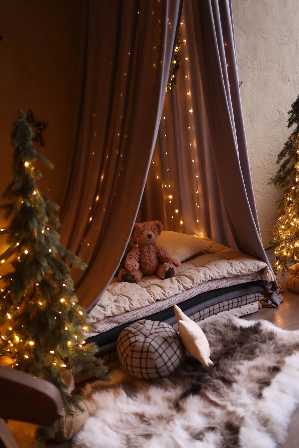 A warm and inviting indoor tent setup with a teddy bear, fairy lights, and plush decor for a serene ambiance.