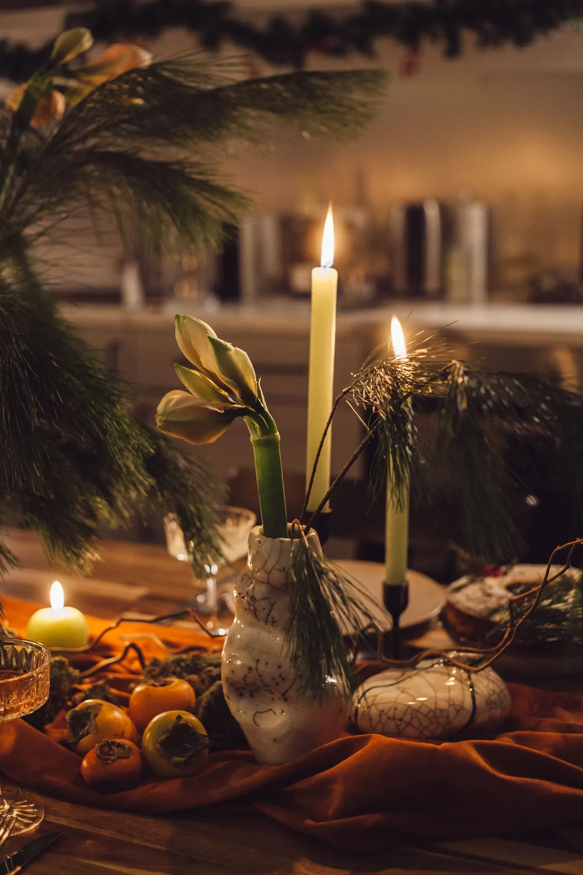 A warm, festive table setting with candles, conifer branches, and decorations, perfect for Christmas ambiance.