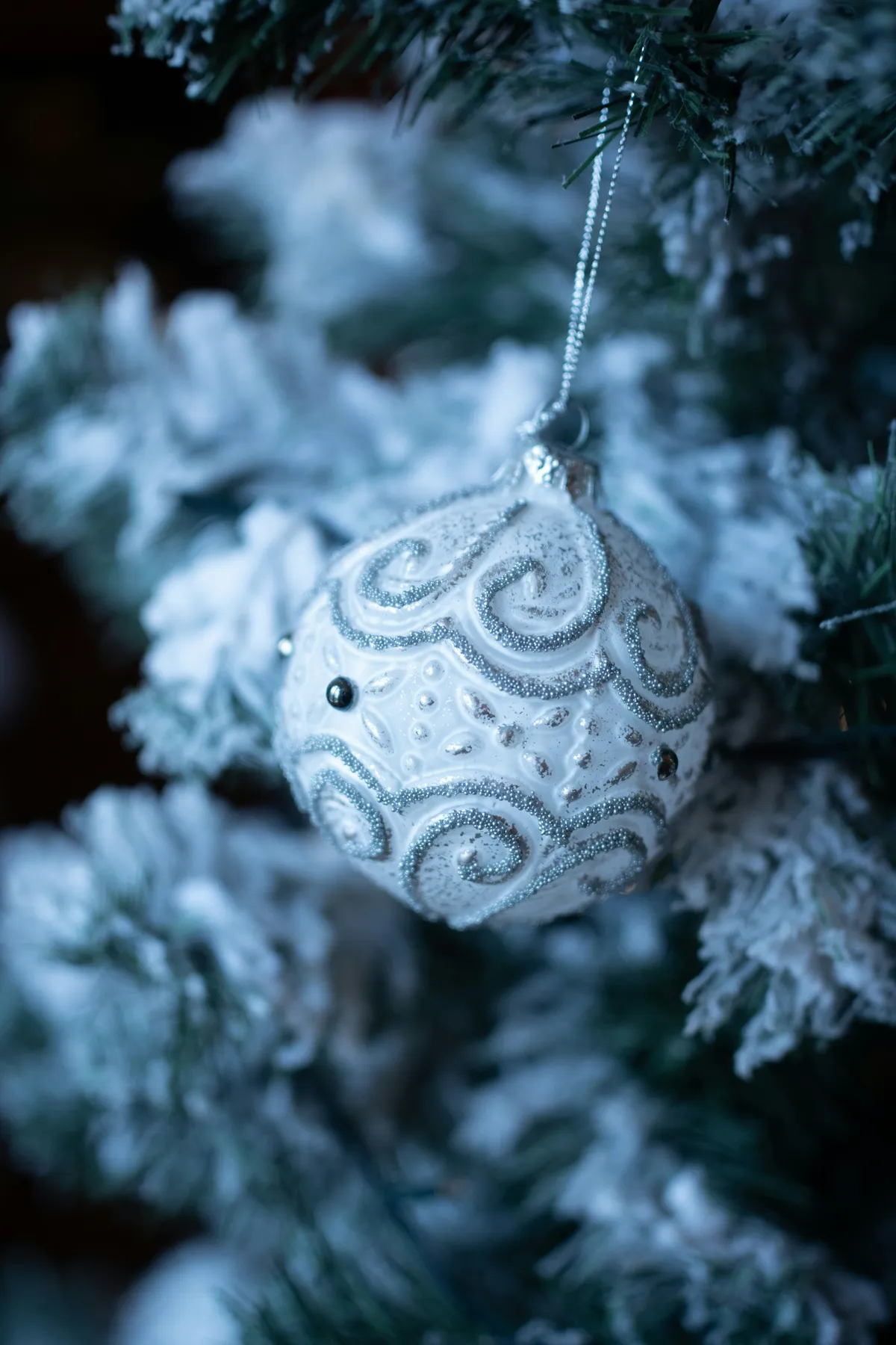 A white christmas ornament hangs on a snowy tree
