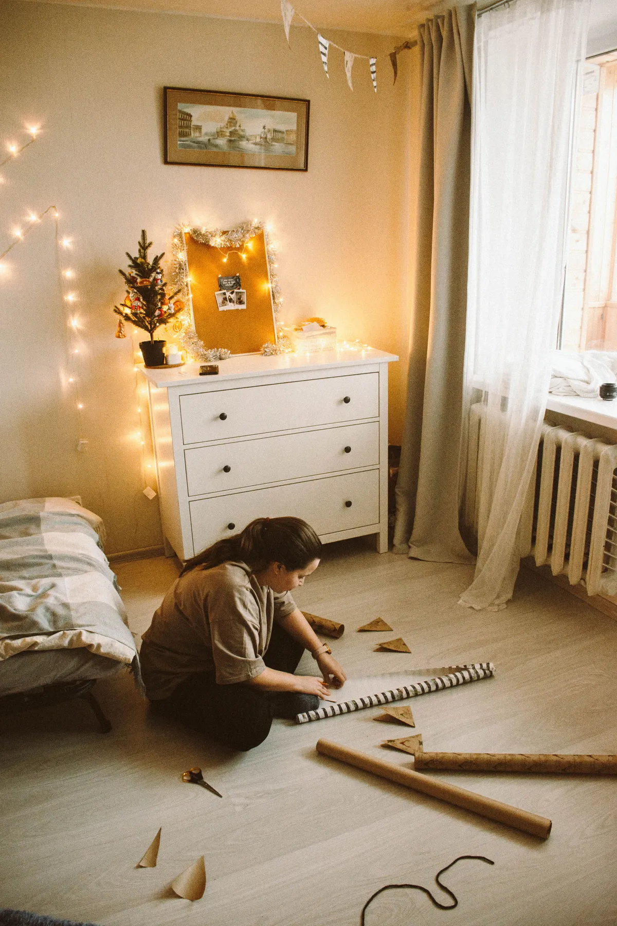 A woman sits crafting on the floor of a festively decorated room with Christmas lights and tree.