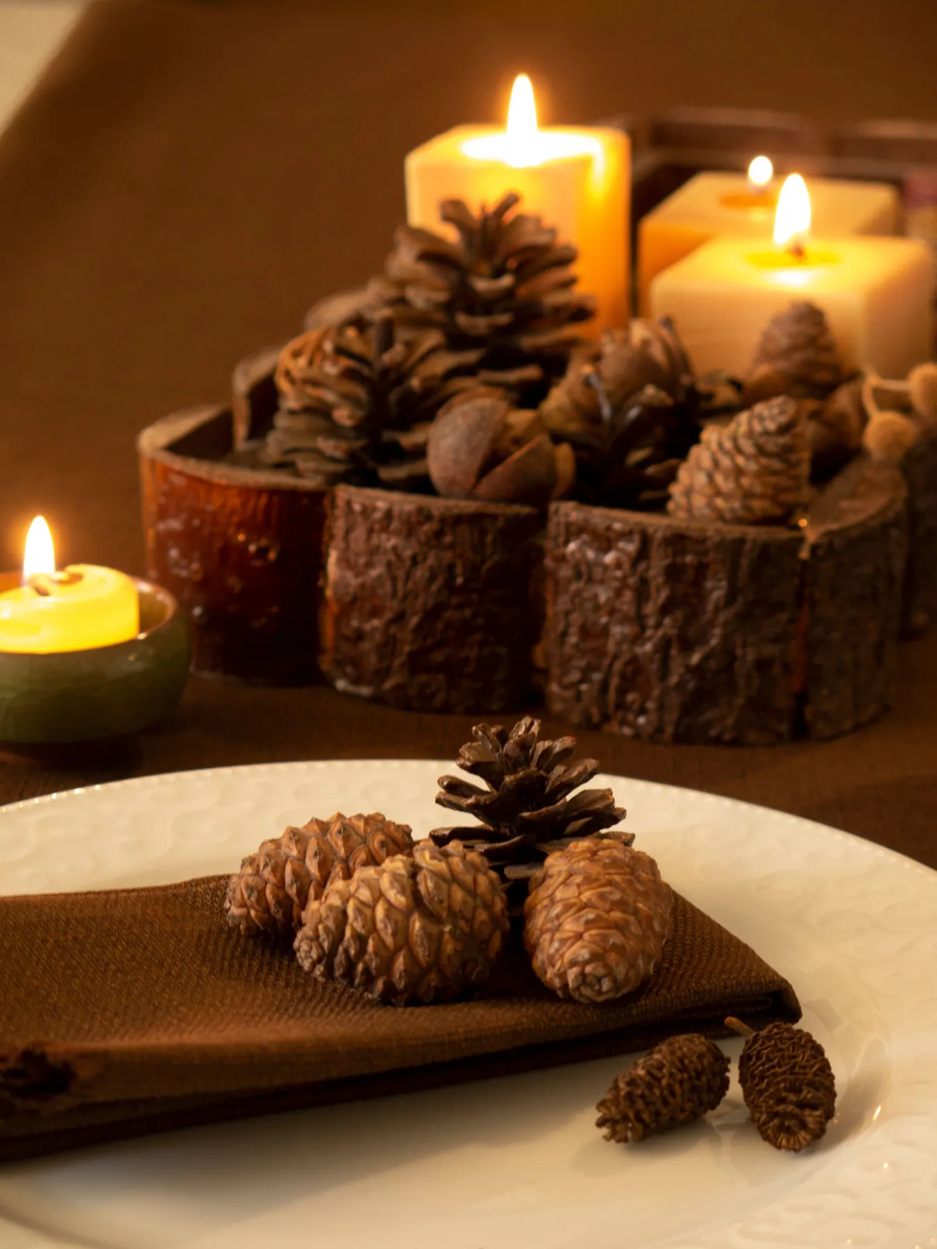 An inviting autumn decoration featuring pinecones and lit candles on a rustic table setting.