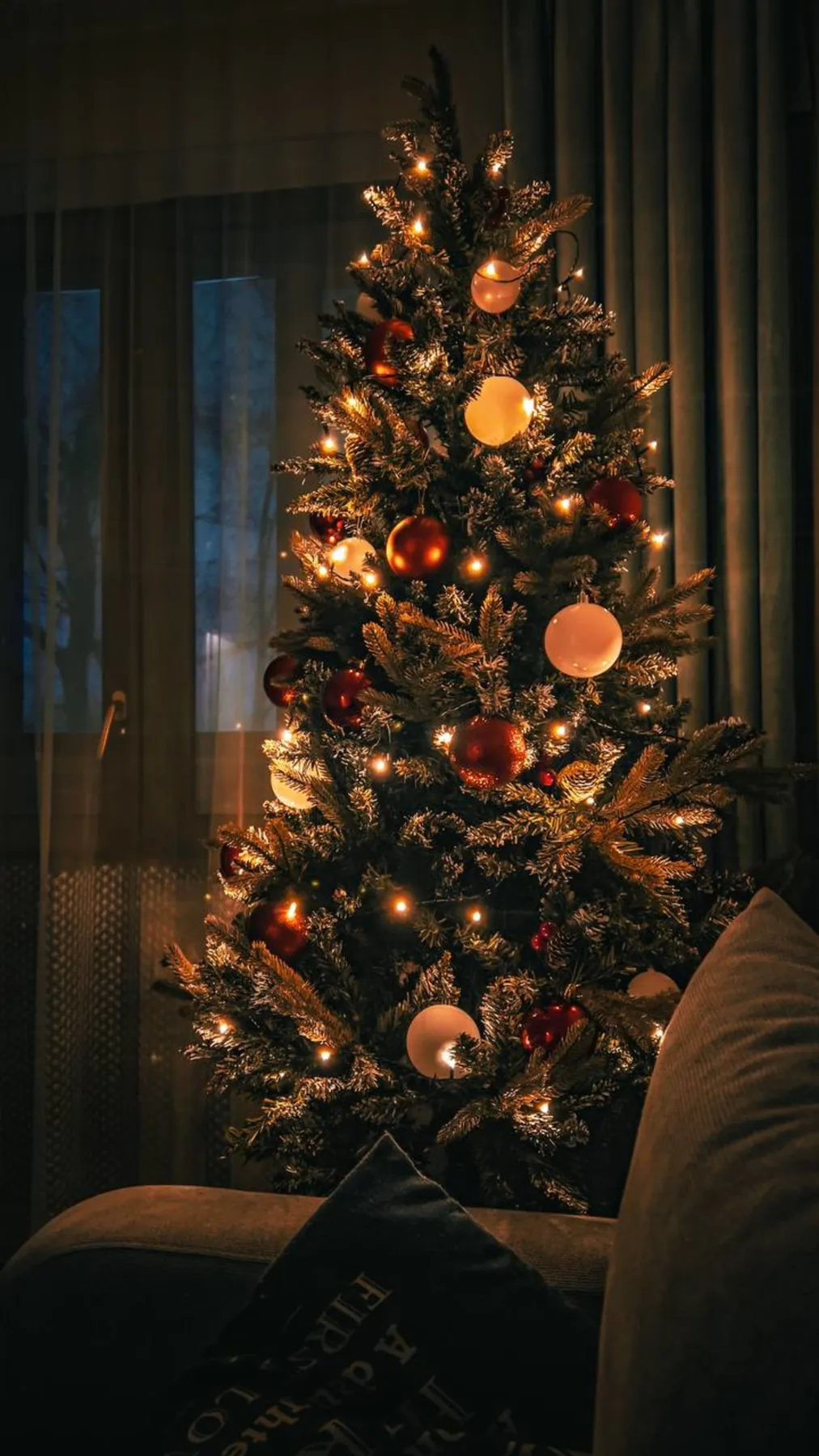 Beautifully decorated Christmas tree with glowing lights in a cozy indoor setting.