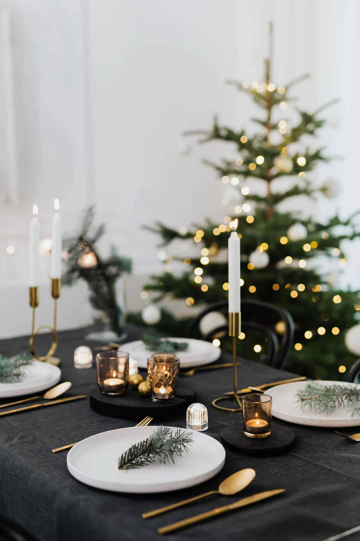 Beautifully set Christmas table with candles and a decorated tree in the background, providing a festive ambiance.