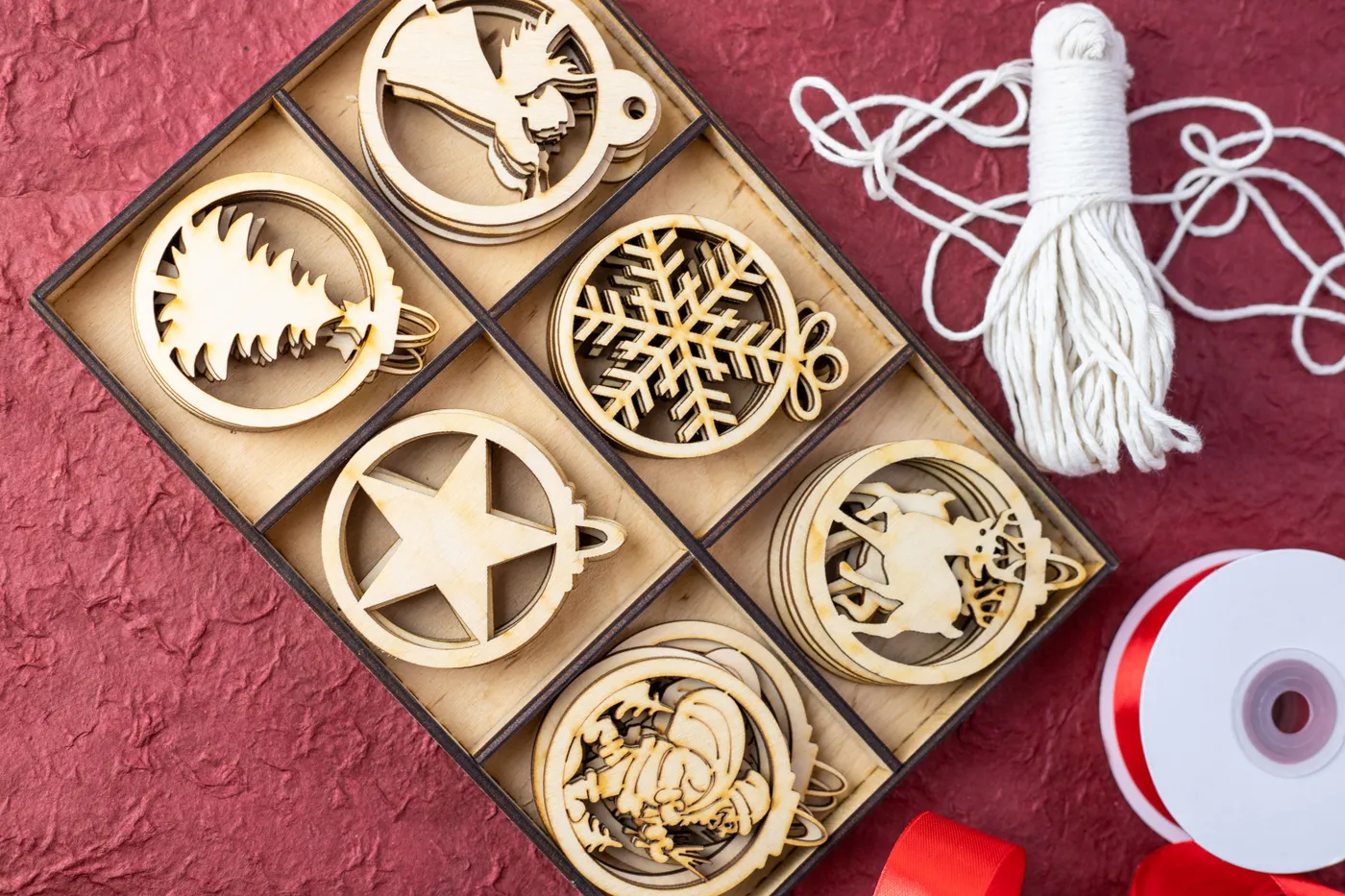 Box of wooden Christmas ornaments with ribbons on red background.