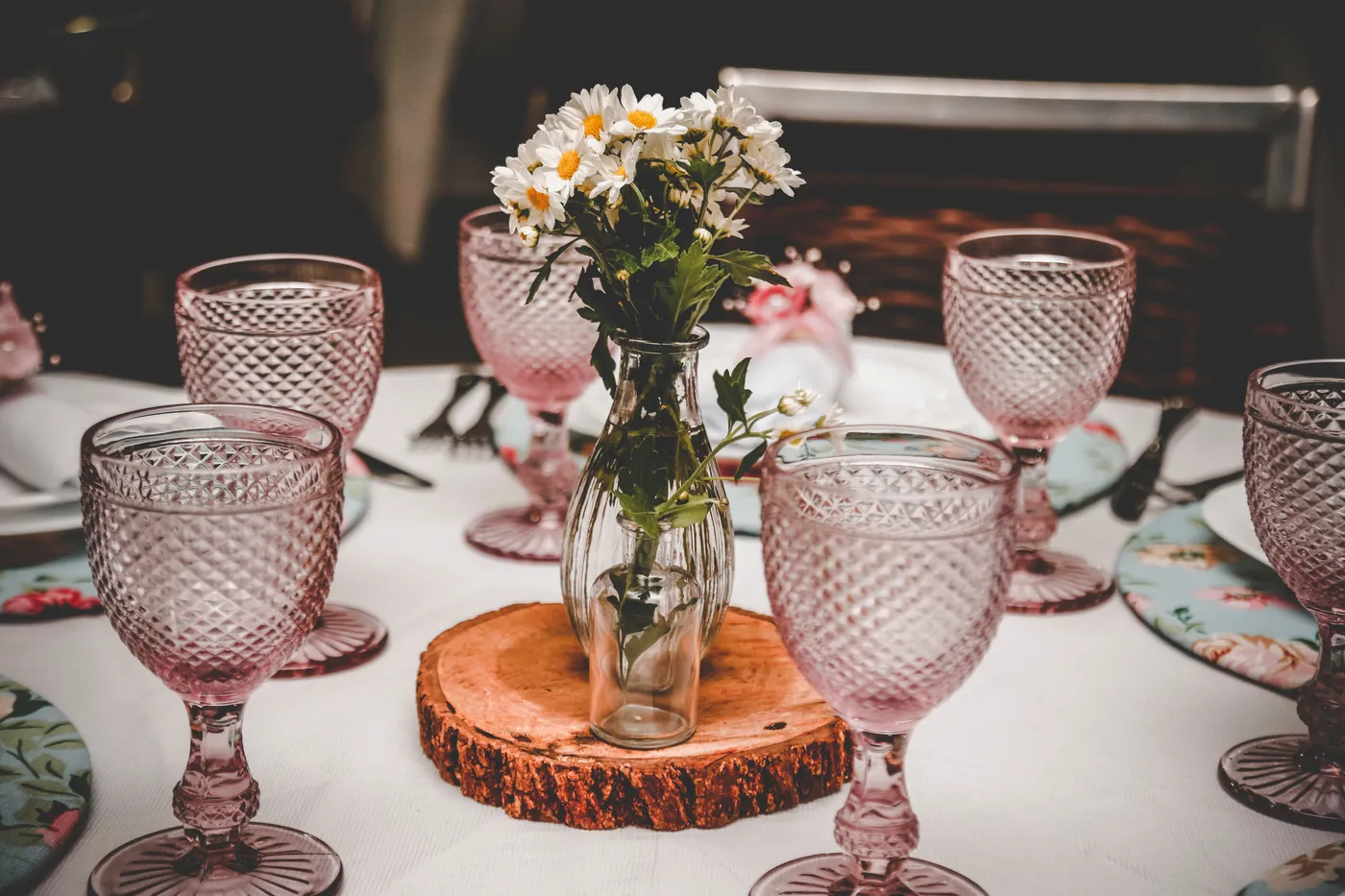 Chic table decor with pink glassware and a rustic floral centerpiece on a wooden slice.