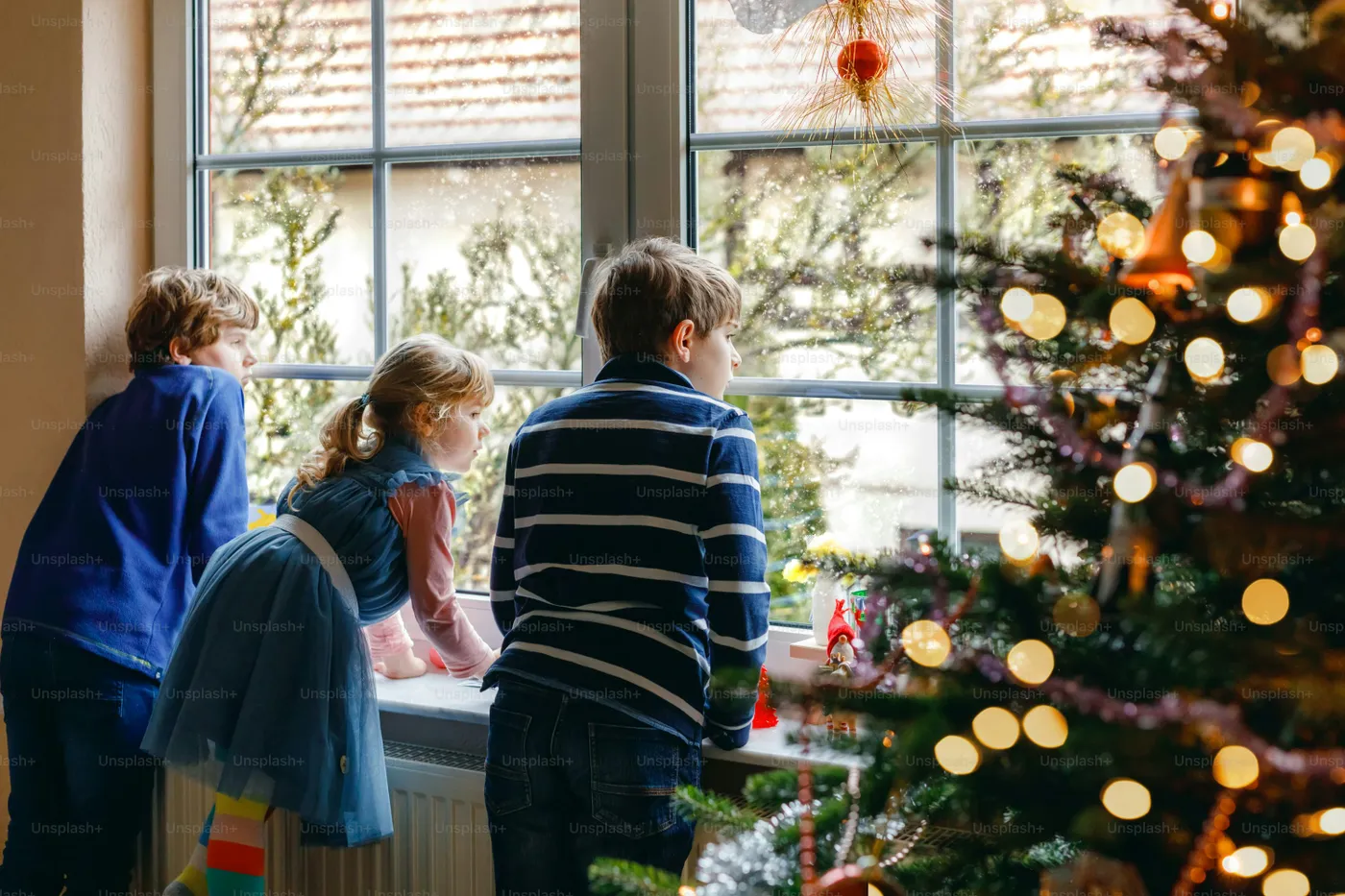 Children looking out window at Christmas - Photo on Unsplash+