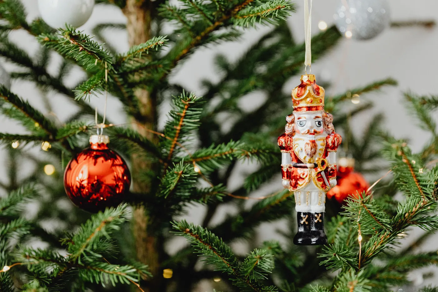 Close-up of a Christmas tree adorned with a nutcracker and red bauble ornaments.