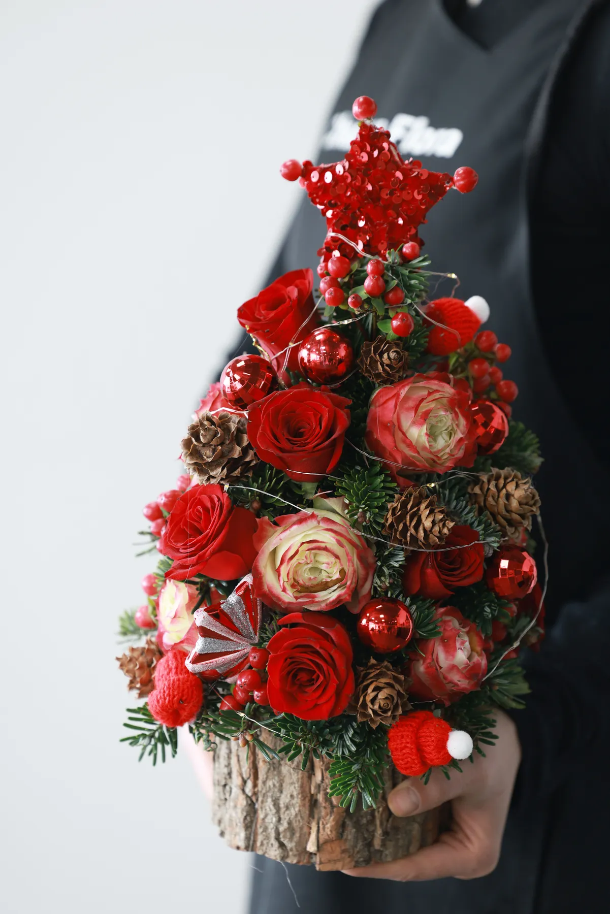 Close-up of a Christmas tree floral arrangement with red roses and pinecones.