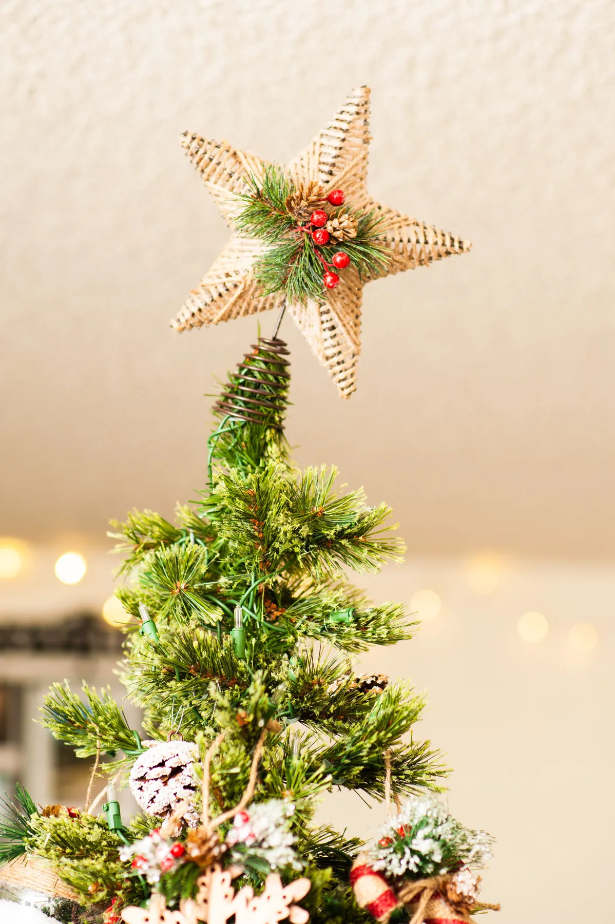 Close-up of a Christmas tree topper featuring a woven star ornament with pine needles and berries.