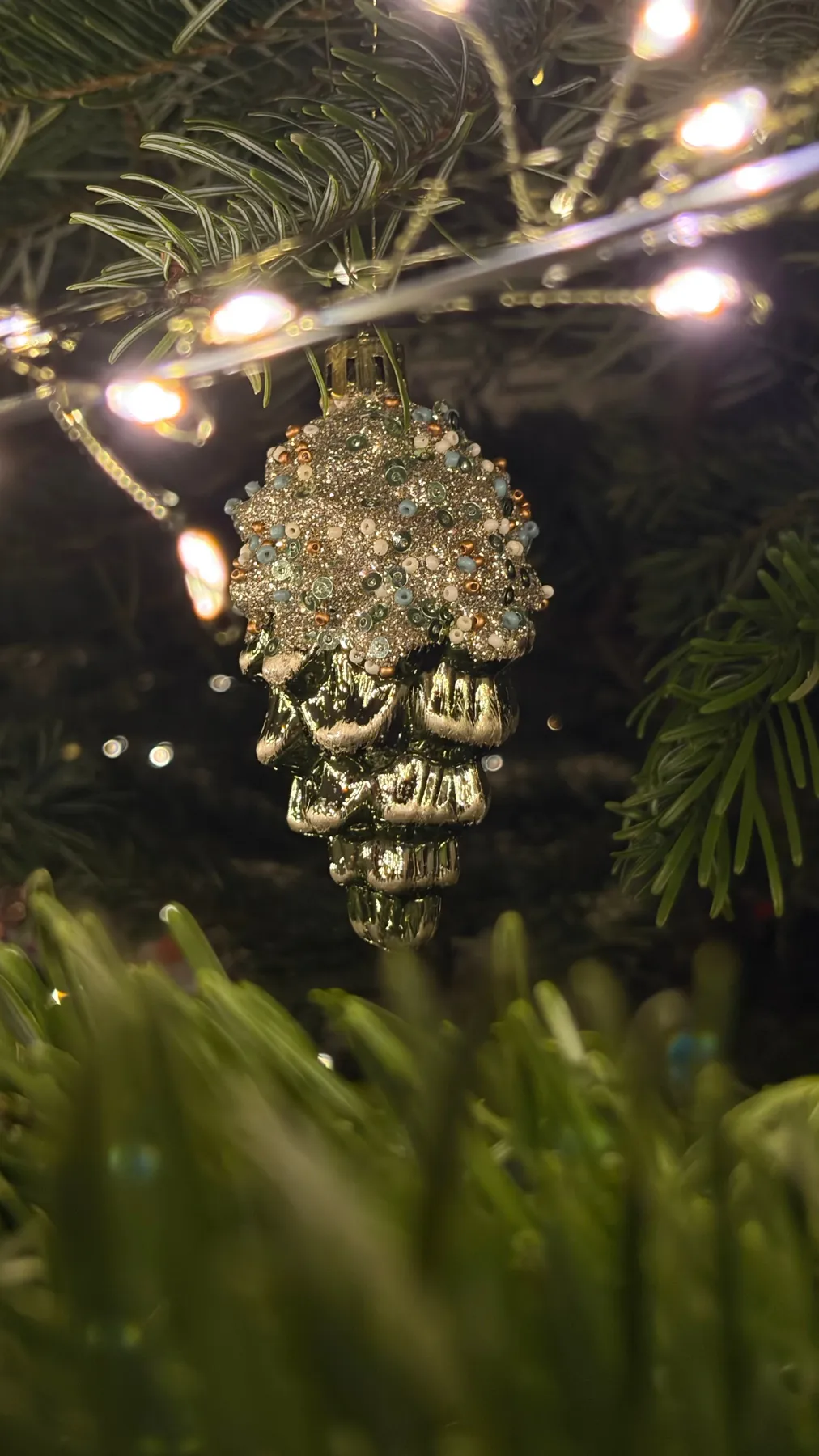 Close-up of a glittering pinecone ornament hanging on a decorated Christmas tree.