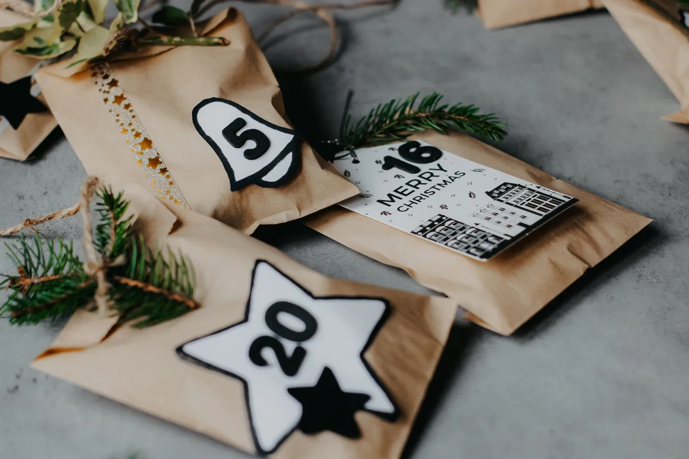 Close-up of Christmas advent calendar with numbered rustic gifts and fir branches on gray background.
