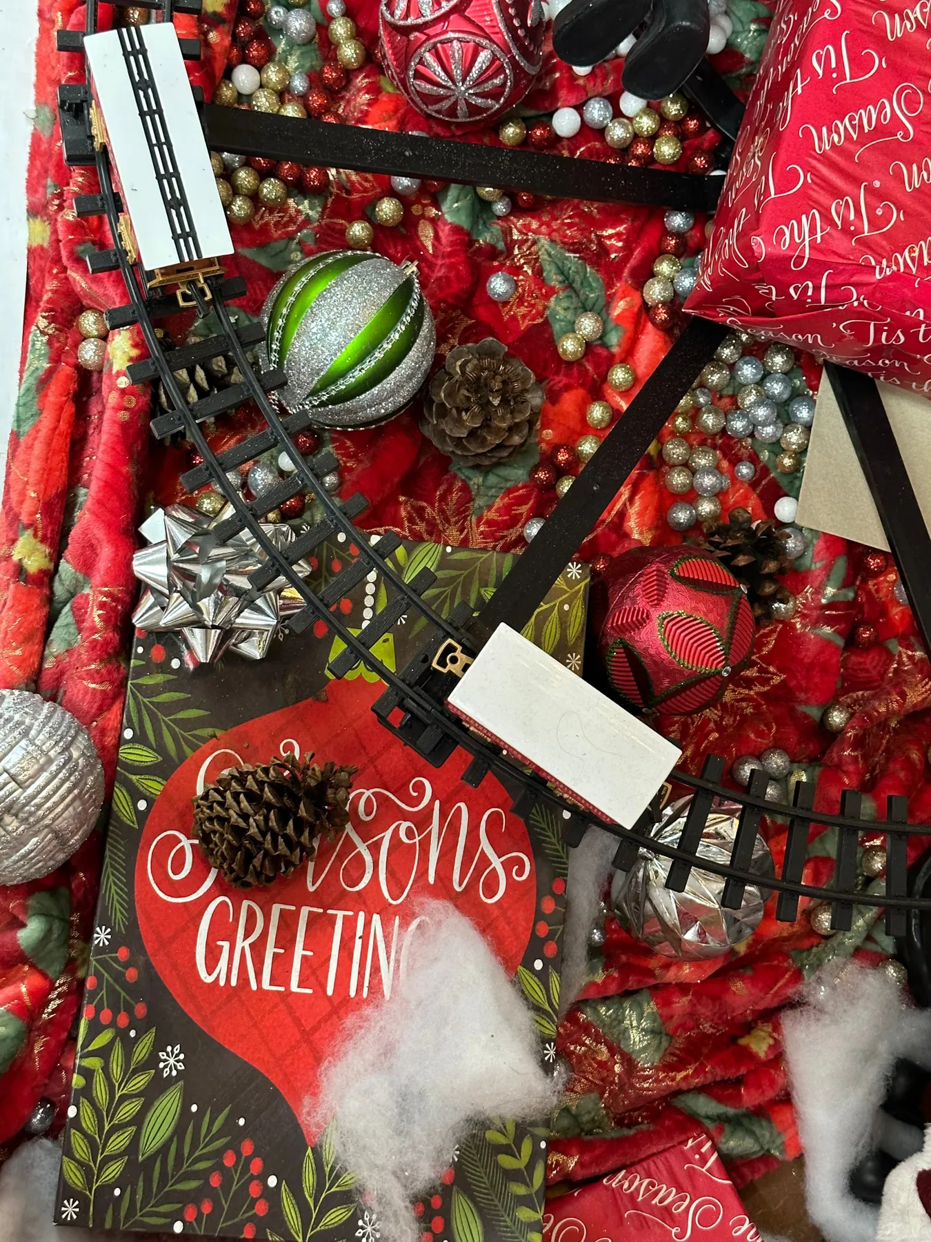 Close-up of Christmas decorations with a toy train set, featuring pine cones and greeting cards.