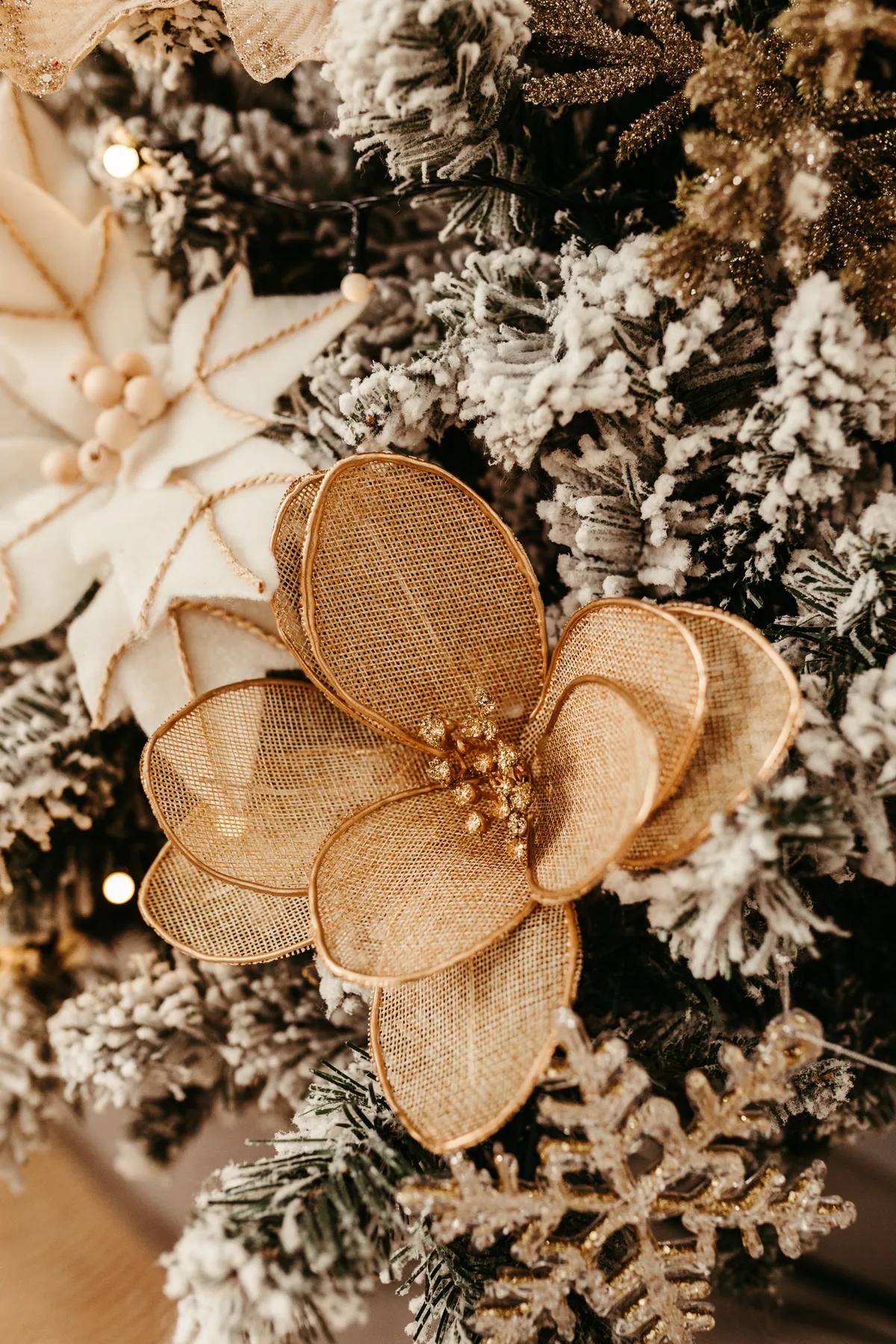 Close-up of gold and white floral decorations on a Christmas tree with snow-dusted branches.