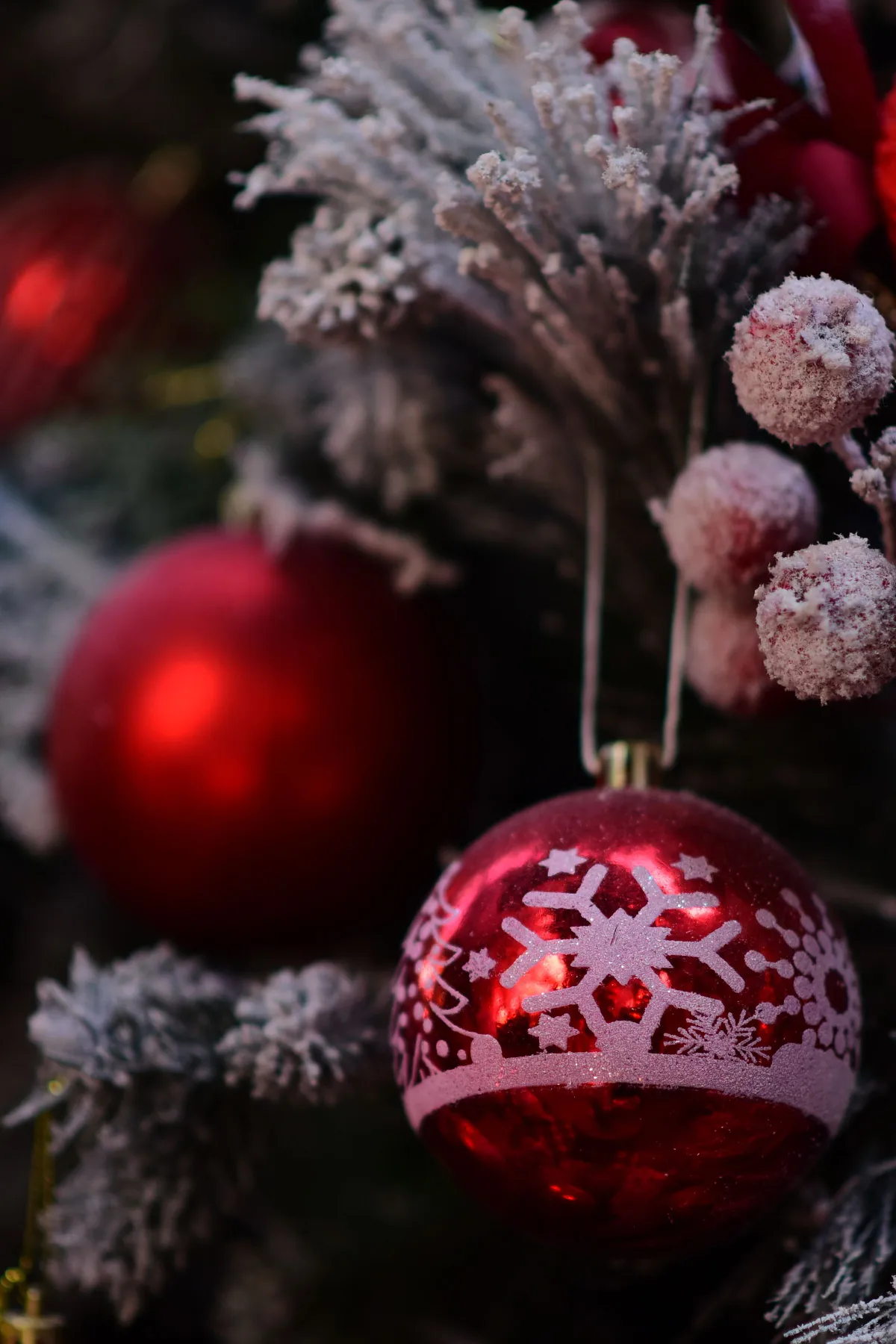 Close-up of red Christmas ornaments with snowflake design on a decorated tree.