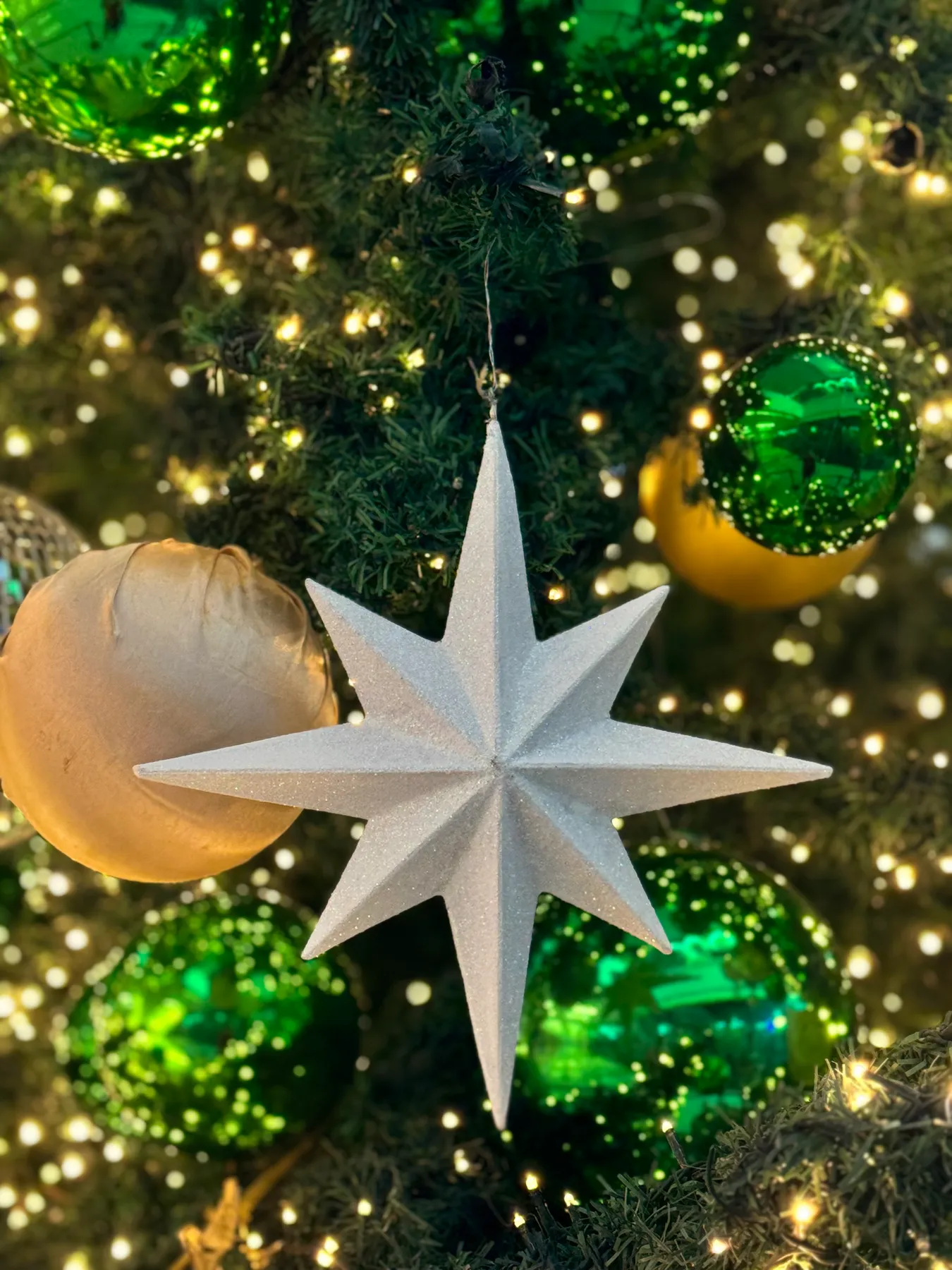 Closeup of a sparkling star ornament on a Christmas tree with green and gold baubles.