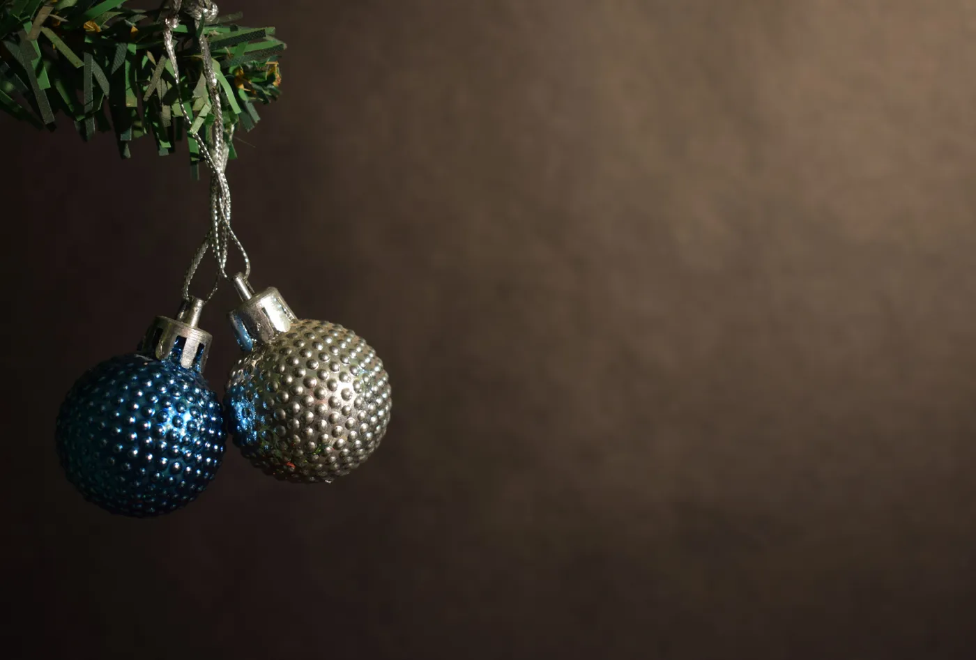Elegant close-up of blue and silver Christmas baubles hanging on a tree branch with a dark background.
