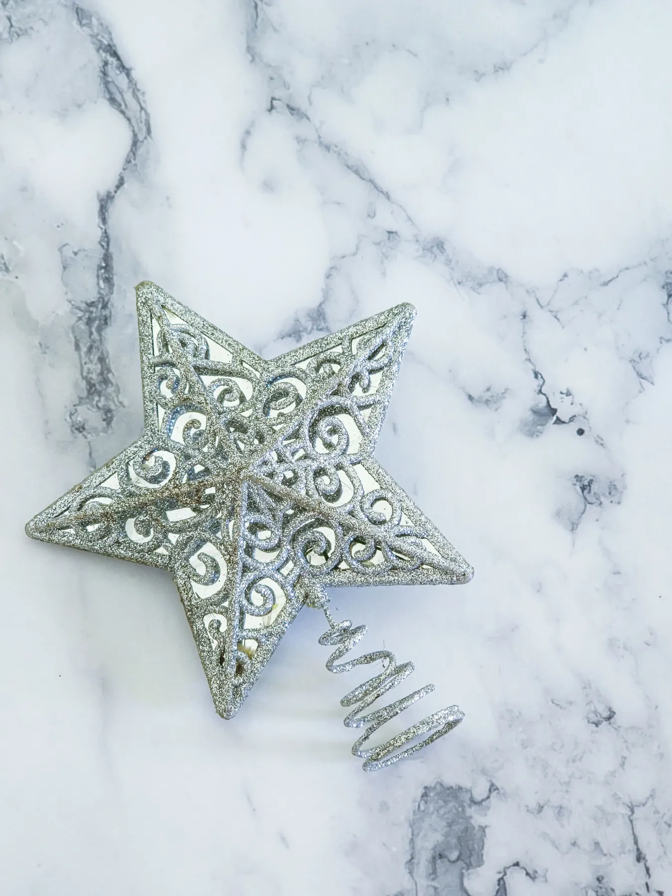 Elegant silver star Christmas tree topper lying on a marble background, capturing holiday spirit.
