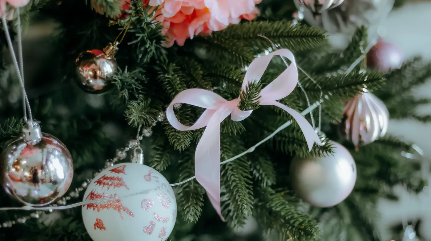 Festive Christmas tree adorned with ornaments and a pink ribbon, creating a joyful atmosphere.