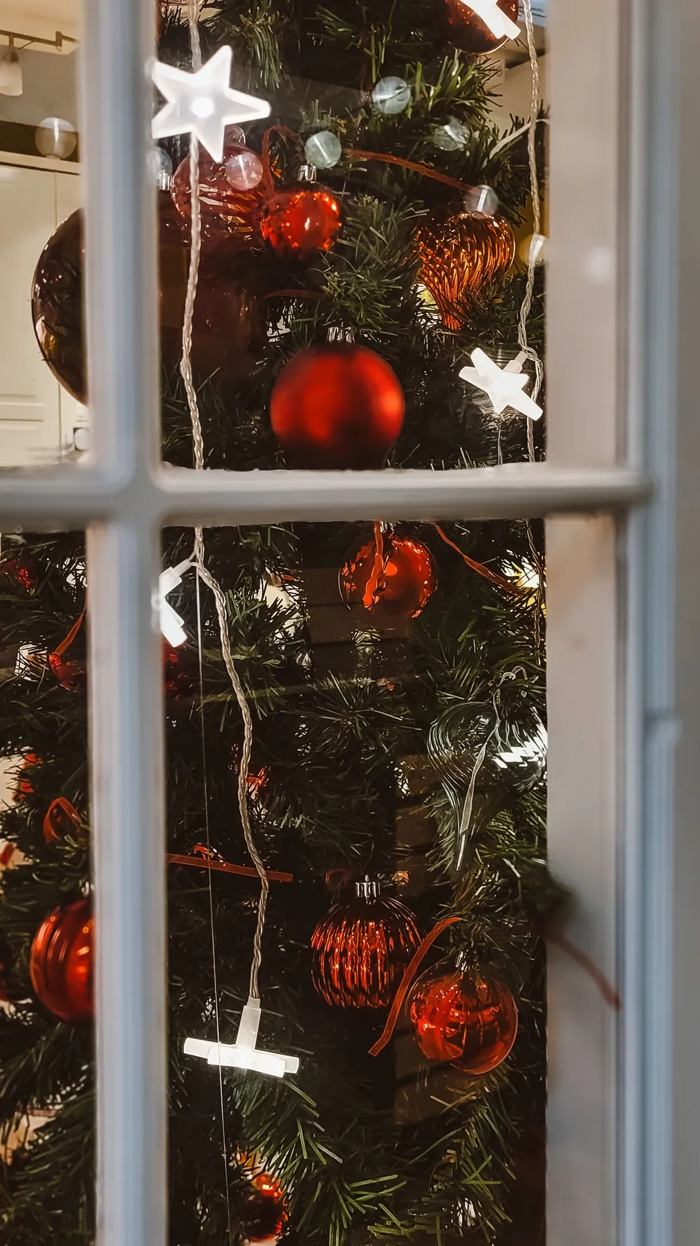 Festive Christmas tree with red ornaments viewed through a window in Ankara, Türkiye.