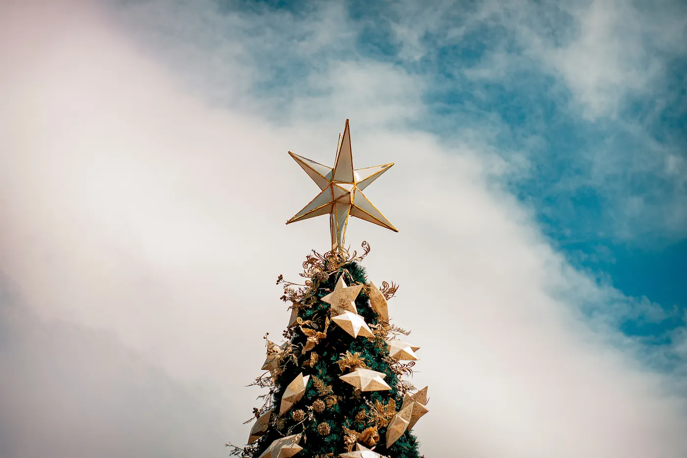 From below Christmas tree edge with golden star on top and decorative baubles against sunny blue sky