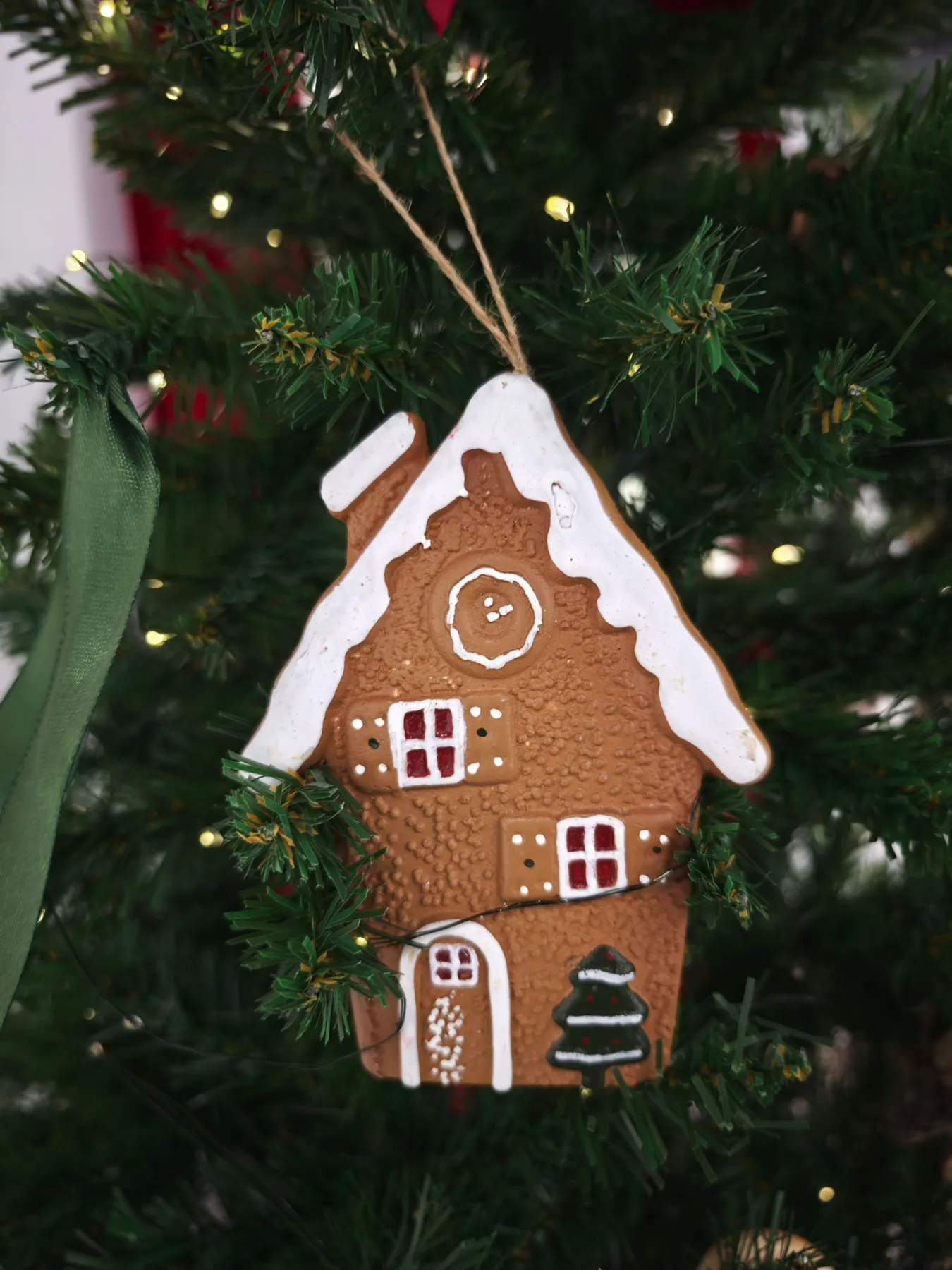Gingerbread house ornament hanging on a decorated Christmas tree with festive lights.