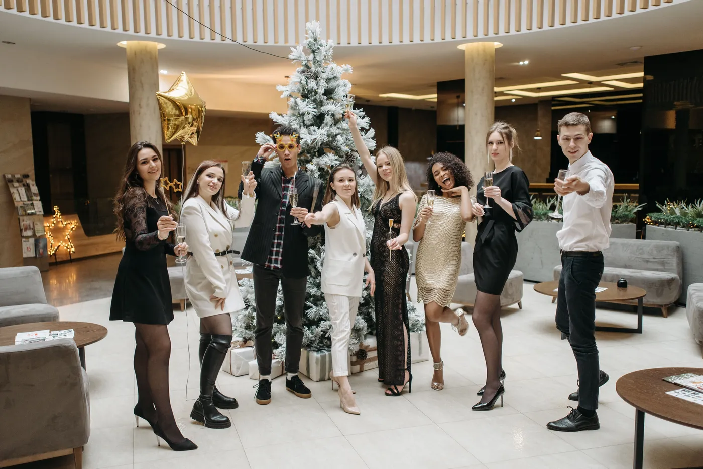 Group of stylish adults celebrating indoors next to a Christmas tree with drinks.