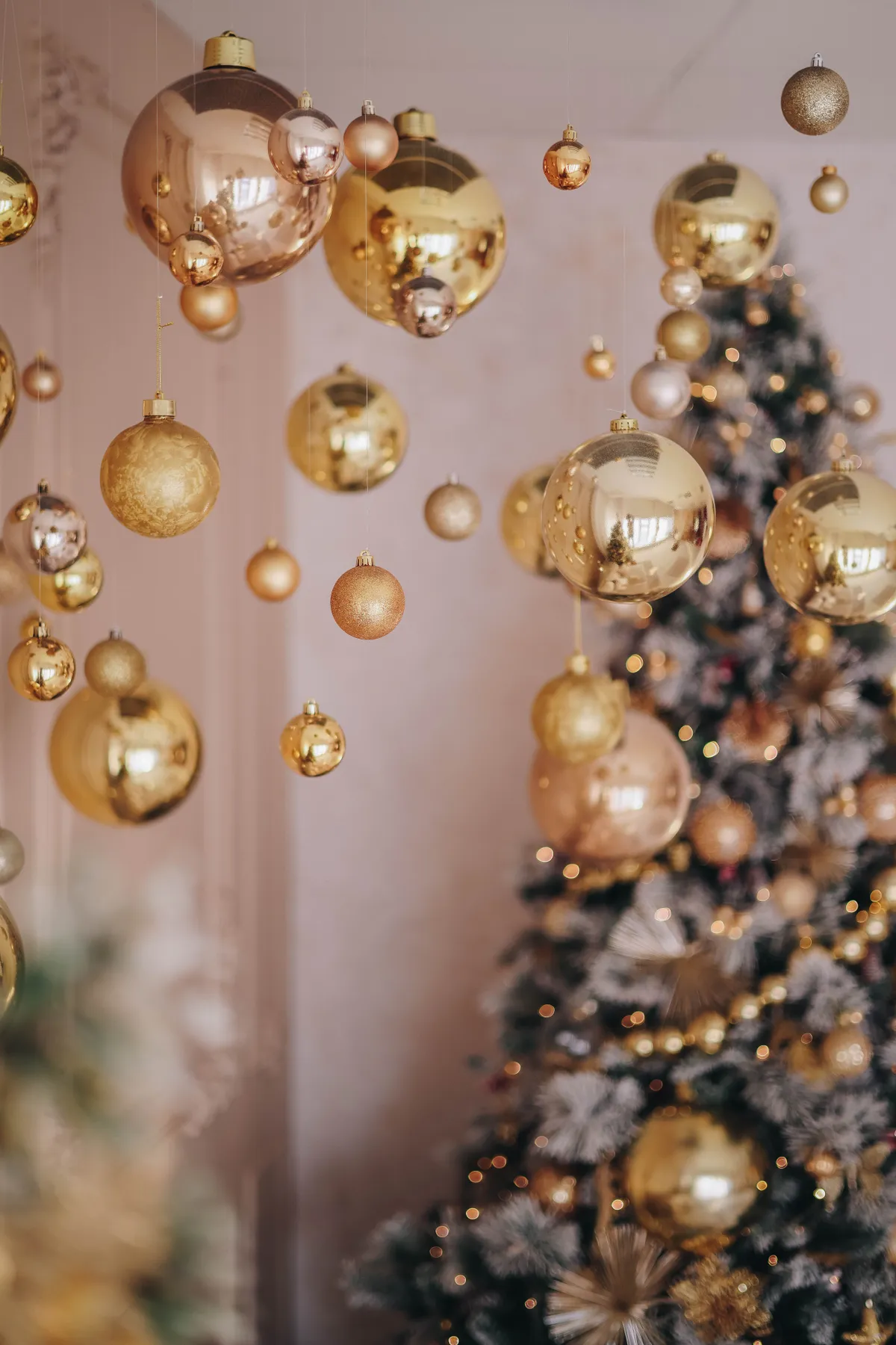 Luxurious golden Christmas ornaments hanging near a beautifully decorated tree.