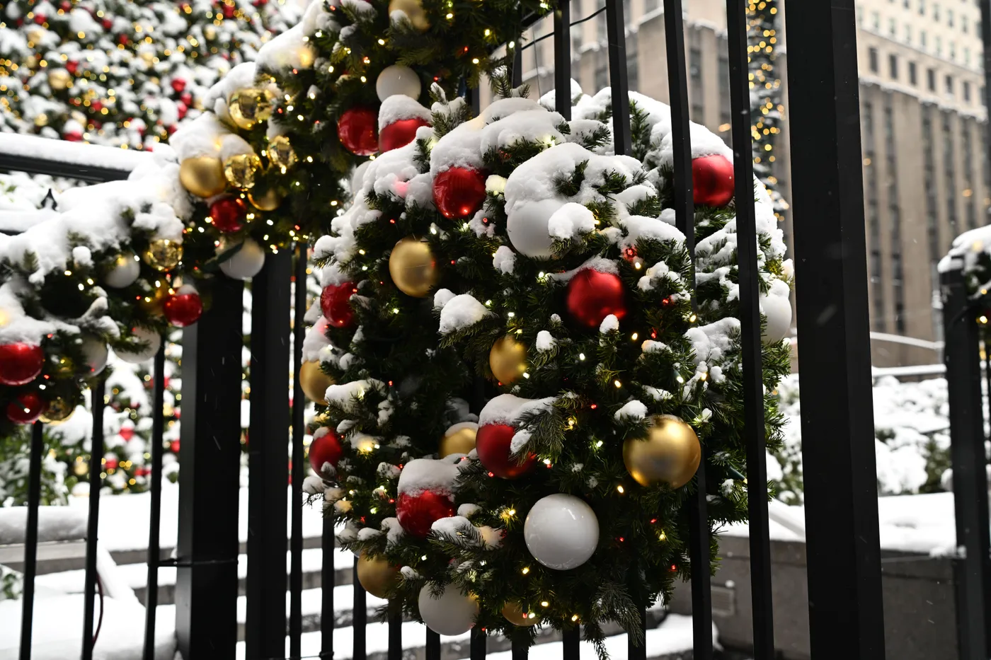 Snow-covered Christmas wreaths adorn a railing in wintery New York City, creating a festive atmosphere.