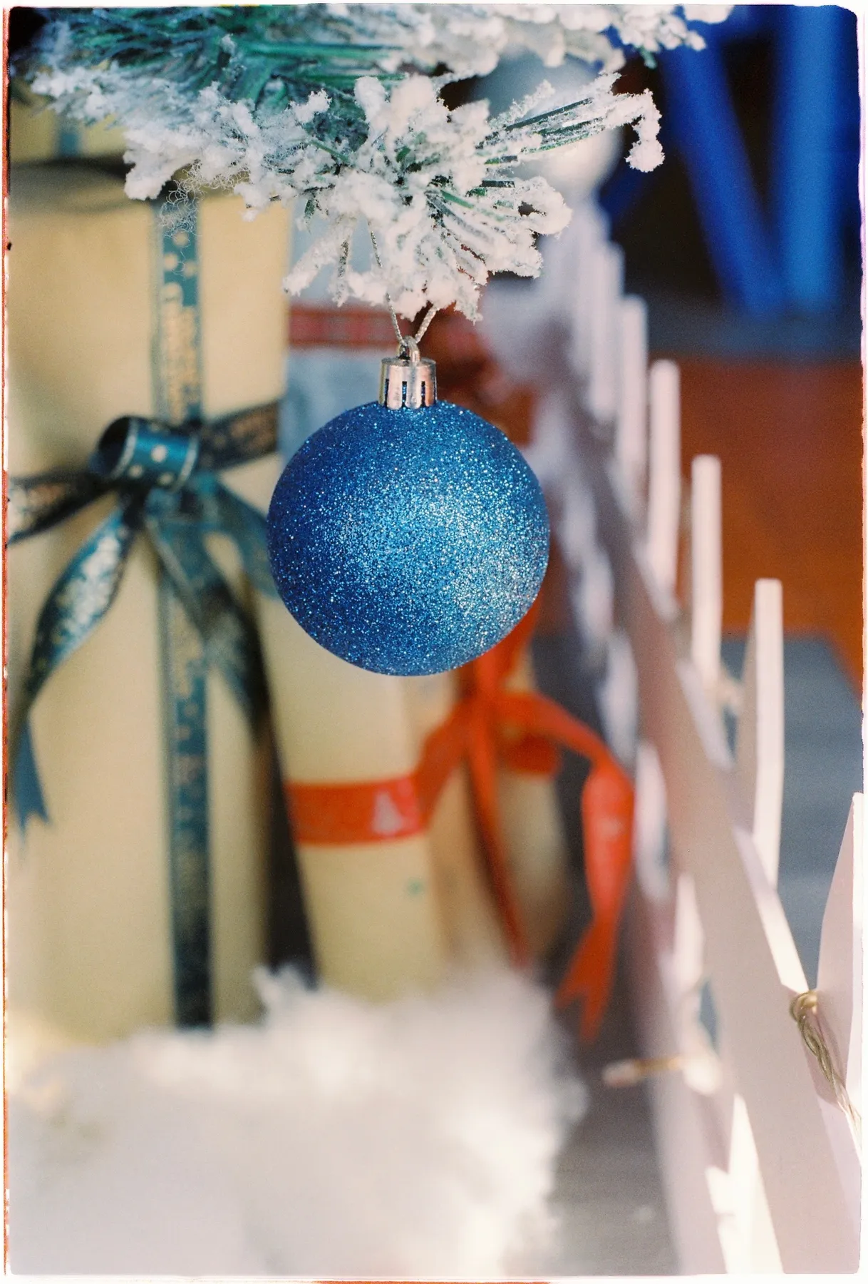 Sparkling blue bauble hanging from a frosted Christmas tree with gifts beneath.