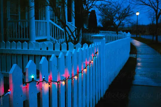 String Of Christmas Lights Hung On A White Picket Fence' by Stocksy  Contributor 'CWP, LLC' - Stocksy