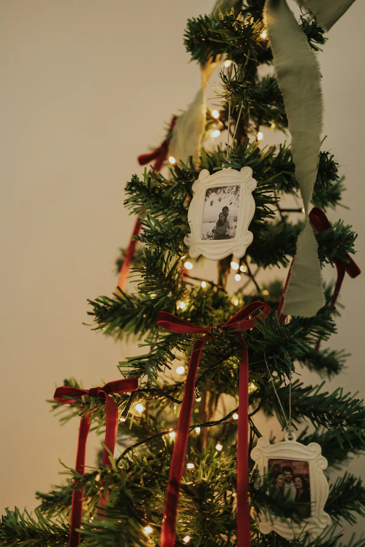 Warmly lit Christmas tree adorned with family photo ornaments and red ribbons, creating a festive atmosphere.